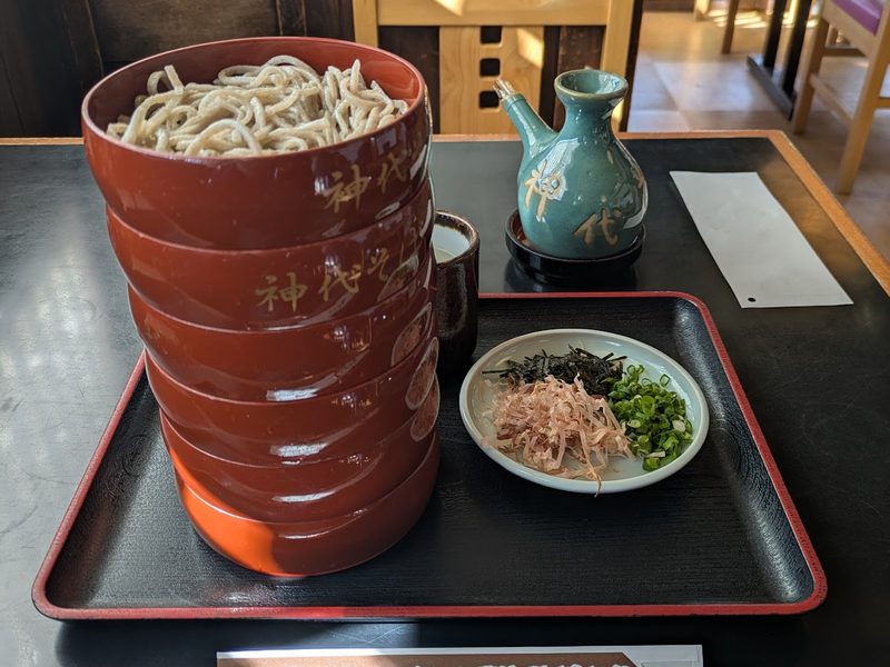 何段も重ねた朱塗りの割子そばと、だしの器、薬味