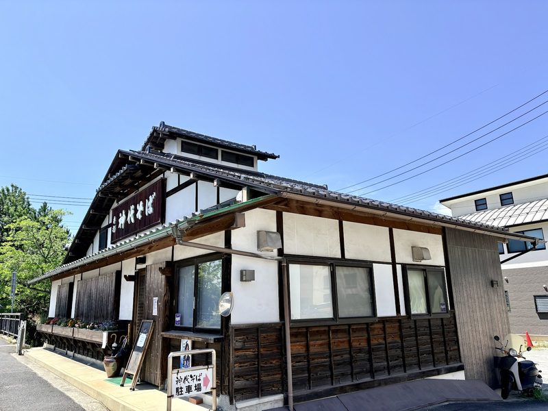 看板を掲げた神代そばの建物を角から見たところ