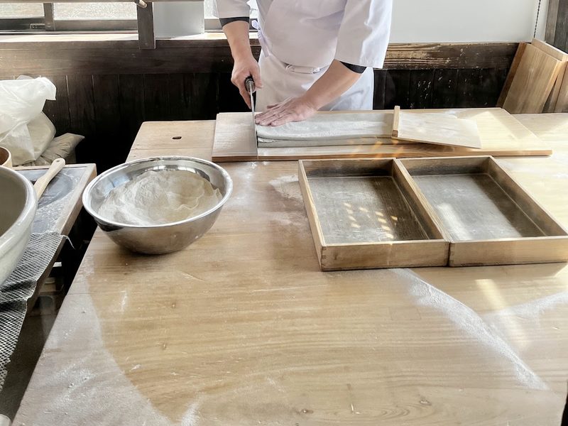 窓辺の作業台でそばを包丁で切っているところ